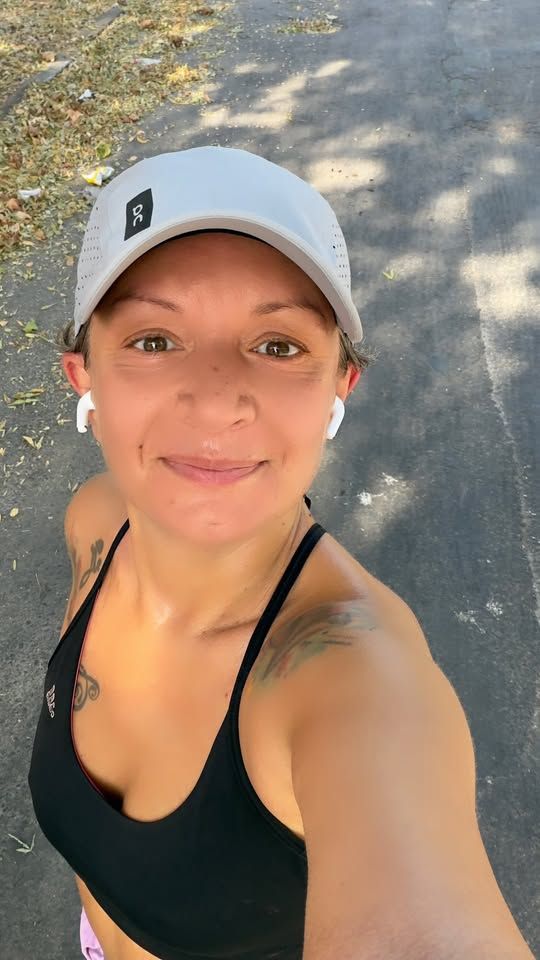 A woman wearing a cap and athletic gear smiles while taking a selfie outdoors after a workout.