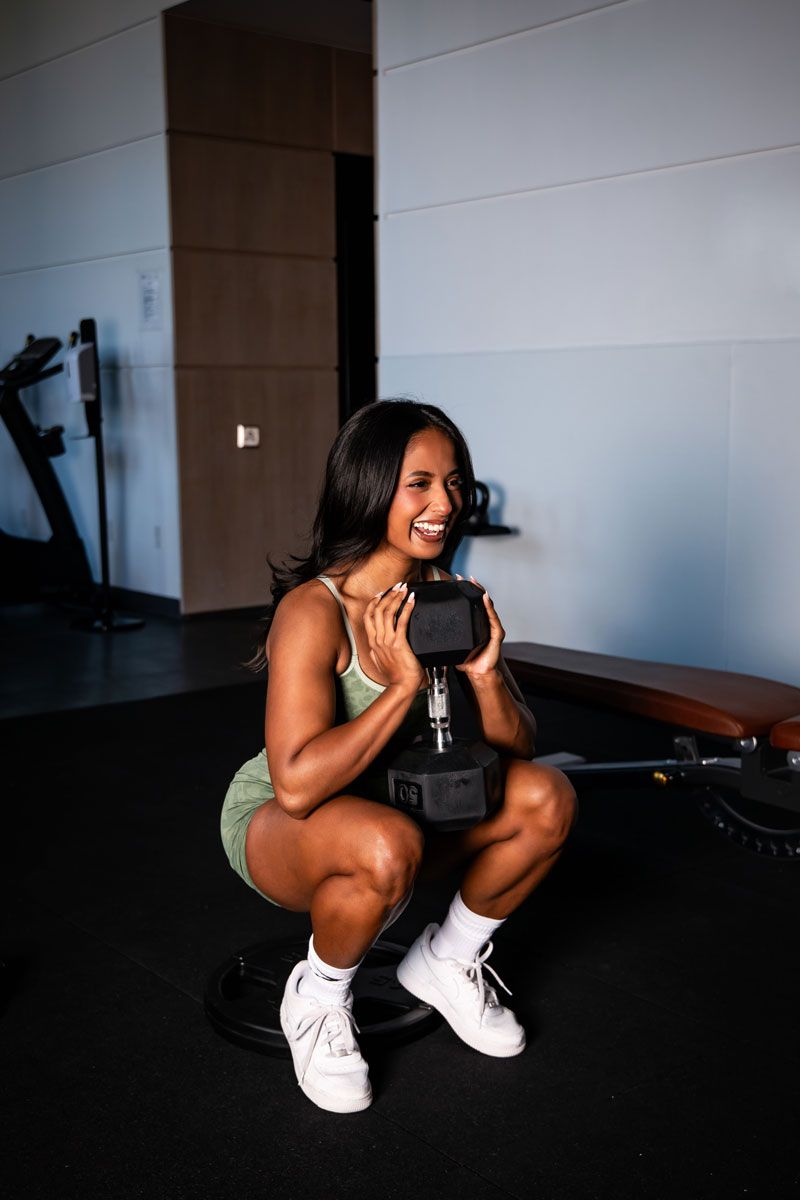 The coach is holding the dumbelle while squating.