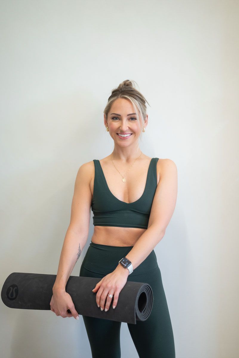The coach is posing while holding the yoga mat.