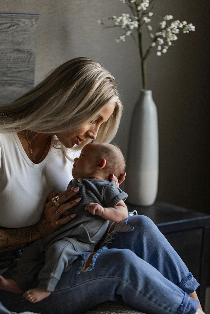 A woman with blonde hair gently holds and looks down at her newborn baby in a dimly lit room.