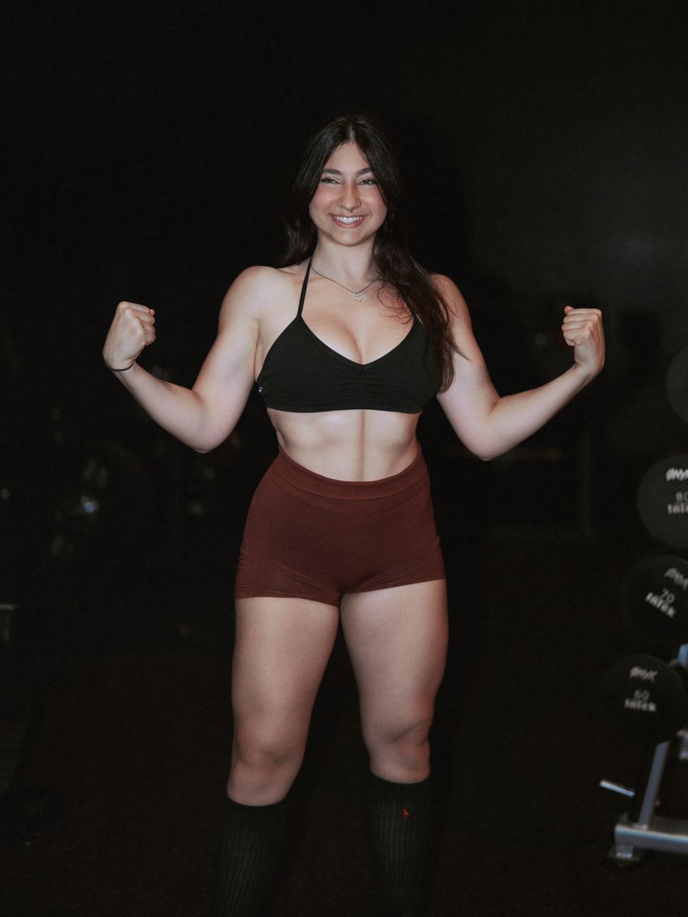 Coach Kacey Green flexing both arms and smiling in the gym